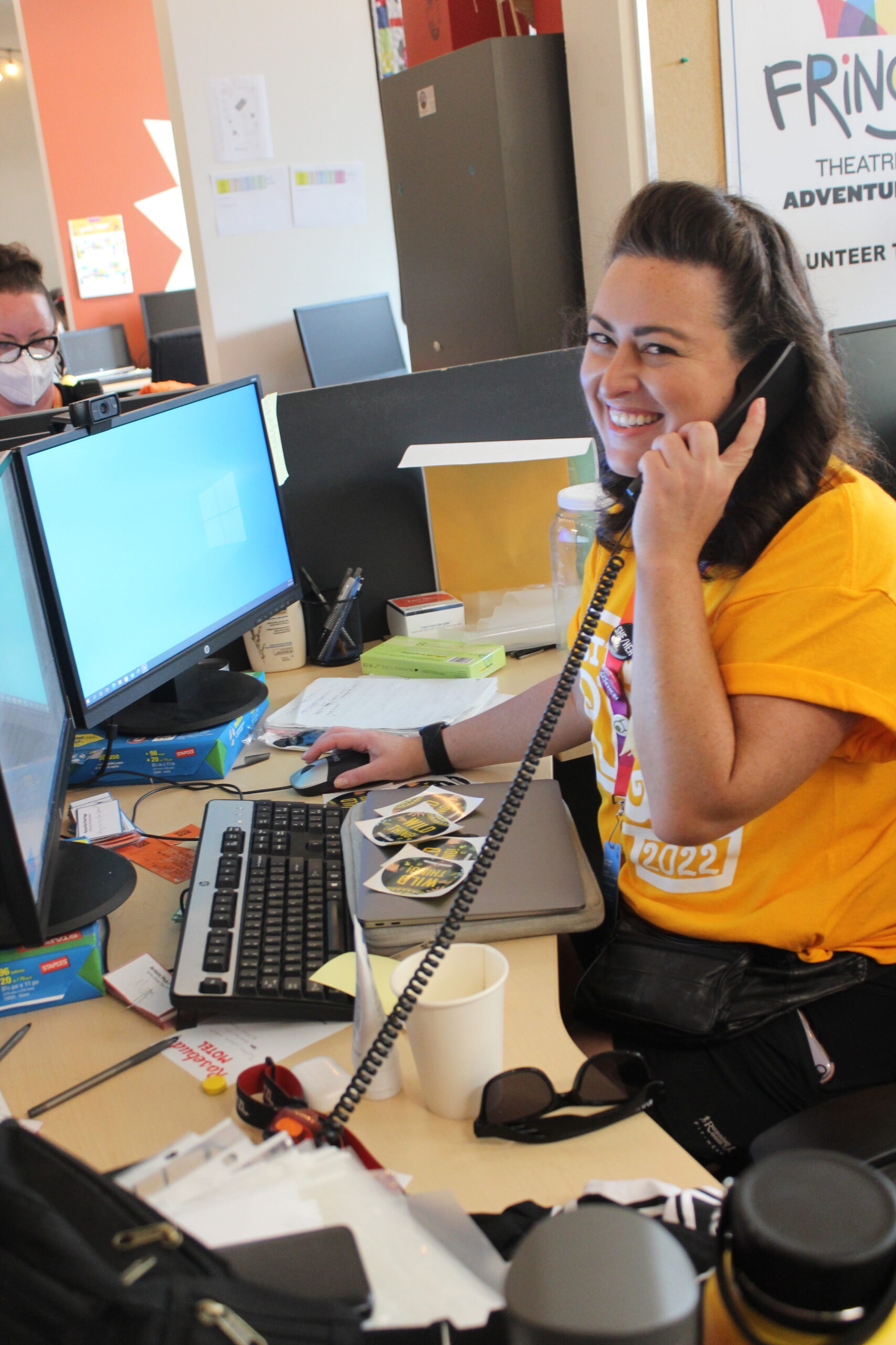 A Volunteer on the phone in front of a computer, smiling.