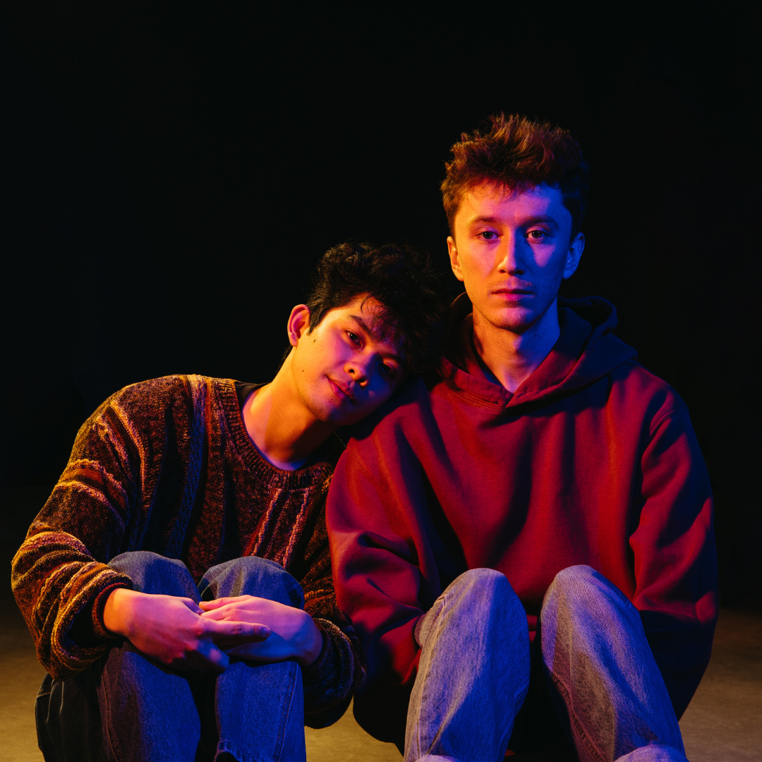 Two young men sit next to each other in dramatic lighting in Mac Brock's 'Boy Trouble,.'