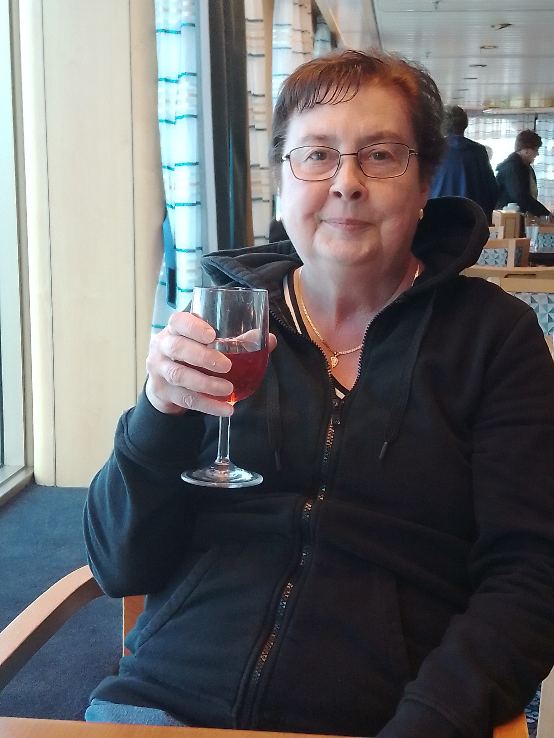 Older woman in black hoodie poses for the camera with a glass of wine. 