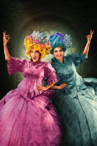Two actors, Christine Lesiak and Tara Travis, are dressed up in flamboyant and colourful ball gowns.