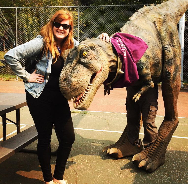 Development Director poses ourtside with a performer wearing a realistic dinosaur costume! 
