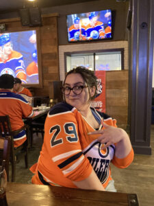 Fringe Programming Coordinator, Victoria deJong, poses in a sports bar with a number 29 Oilers Jersey. 