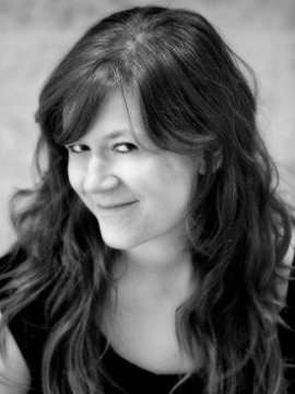 A woman in black-and-white looks side-eyed at the camera with a closed-lip smile.