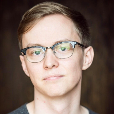 A man in horn-rimmed glasses regards the camera with a close-lipped expression.