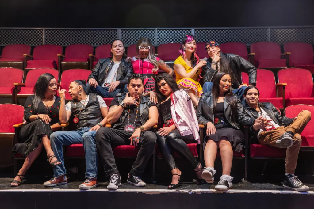 The cast of "Bear Grease" sit in red theatre seats.