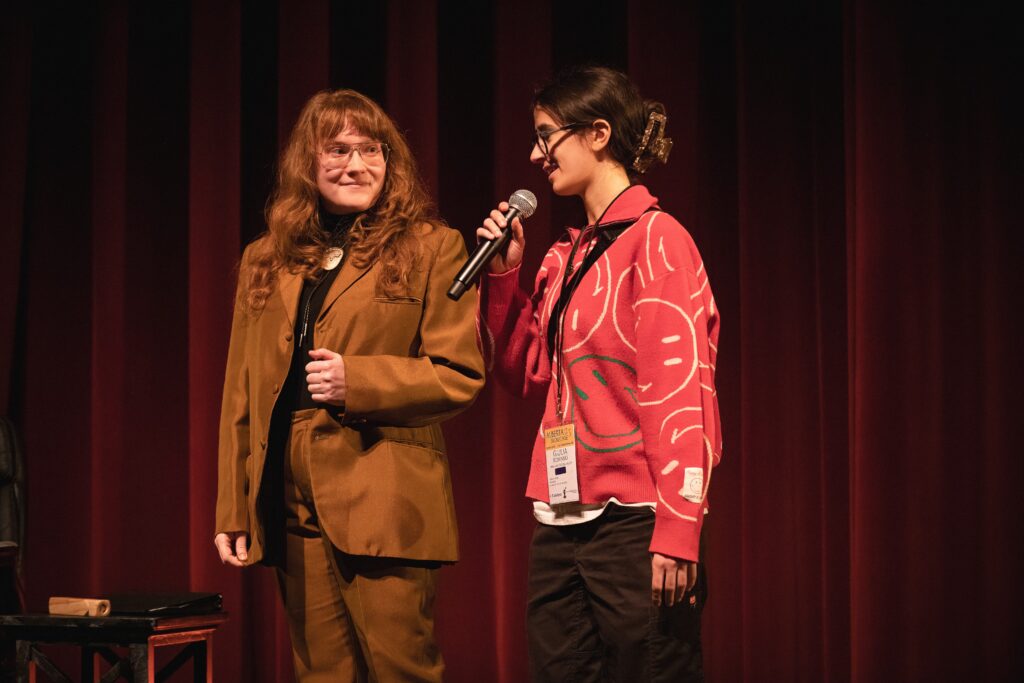 AJ and stands next to another artist who is speaking into a microphone.