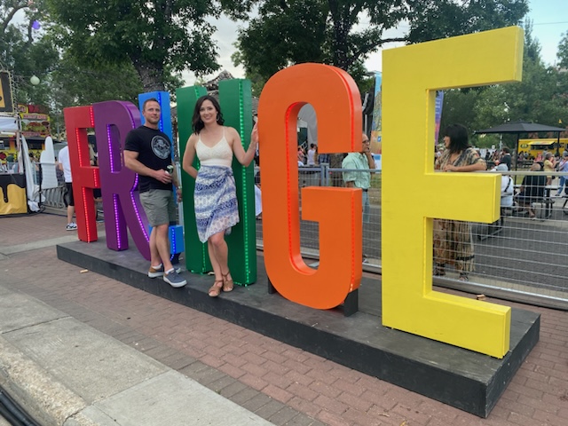 Two people stand next to the giant Fringe sign.